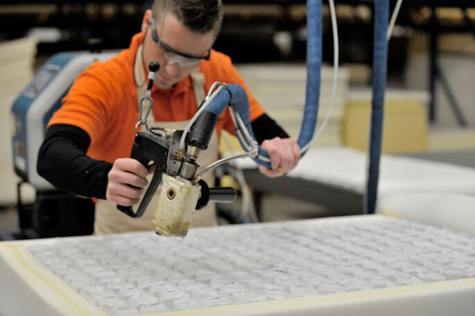 Man applying manual hotmelt adhesive on mattress